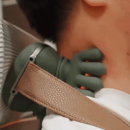 Person wearing a green neck massager with a brown strap over a white shirt